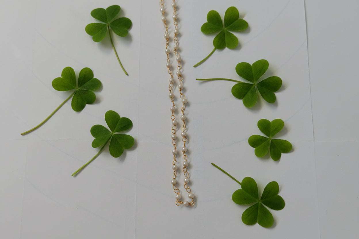 Gold necklace with green clover leaves on a white background