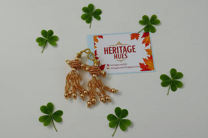 Gold earrings on a 'Heritage Hues' branded card with autumn leaves design.