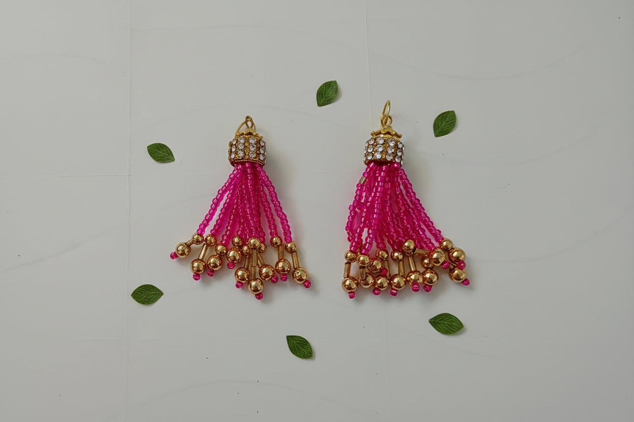 Pair of pink beaded tassel earrings with gold accents on a light gray background