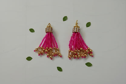 Pair of pink beaded tassel earrings with gold accents on a light gray background