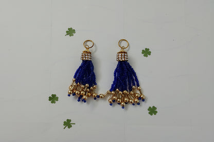 Two blue tassel charms with gold accents on a white background
