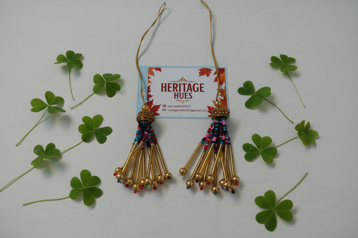 Gold tassel earrings with colorful beads on a white background with shamrock leaves and a 'Heritage Hues' card.